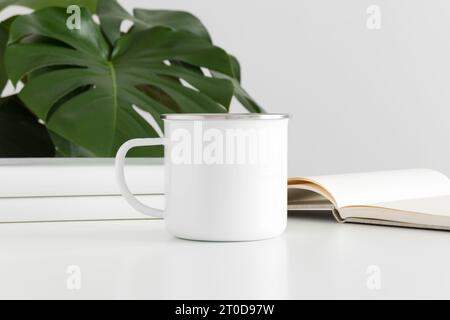 Enamel mug mockup with workspace accessories and a monstera plant. Stock Photo