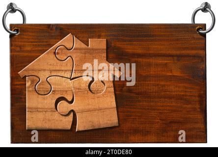 Wooden sign with a wooden house made of puzzle pieces and copy space, and steel rings for hanging. Isolated on white background and copy space. Stock Photo