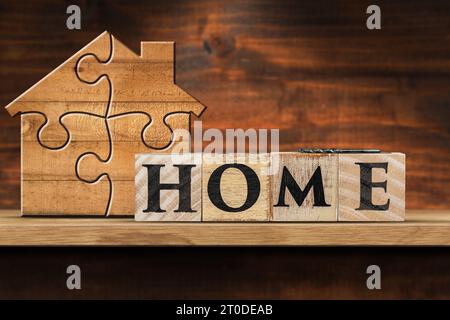 Wooden house made of puzzle pieces and text Home made of wooden blocks, on a wooden shelf with copy space. Stock Photo