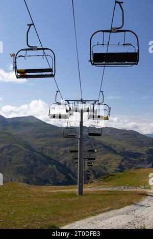 An empty ski chair lift in the summer, high up in the mountains landscape and blue sky background. Ski resort Valloire in France. Copy space below. Stock Photo