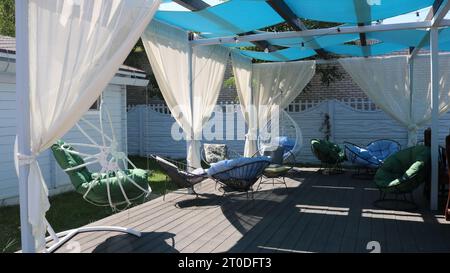a private relaxation area on the sun terrace with comfortable chairs and wicker swings, the use of light light textiles in the interior design Stock Photo