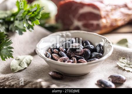 Fresh legume beans in a bowl and smoked pork neck in the background. Stock Photo