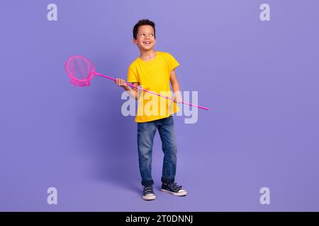 Full size photo of cute young schoolboy hold fishnet look empty space wear yellow clothes isolated on purple color background Stock Photo