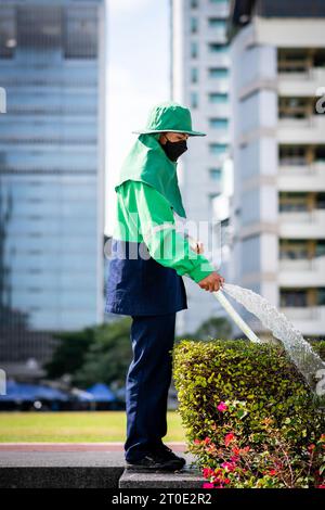A Thai gardener uses a hosepipe to water a hedge on the grounds of Srinakharinwirot University Bangkok, Thailand. Stock Photo
