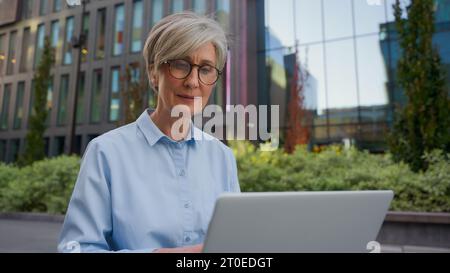 Caucasian middle aged mature woman senior old businesswoman office manager architect developer business lady working online in city typing on laptop Stock Photo