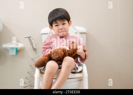 Asian boy Sitting on the toilet bowl in hand holding teddy bear Stock Photo