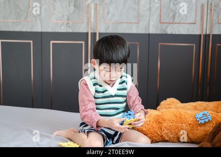 Asian boy playing with jigsaw puzzles on the bed joyfully Stock Photo