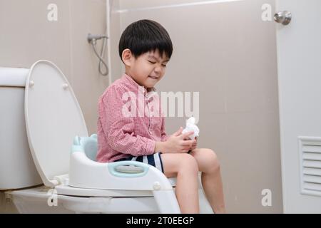 Asian boy Sitting on the toilet bowl in hand holding tissue Stock Photo