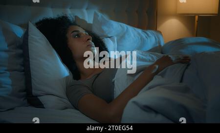 Noisy neighbours problem annoyed African American woman lying in bed night dark bedroom suffer from sleeping disorder insomnia sleepless angry girl Stock Photo