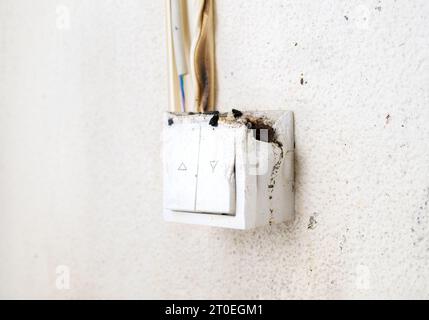 Melted light switch with fire damage, close up. Light regulator mounted on wall caught on fire. Yellow stained wall, with black burn marks. House fire Stock Photo