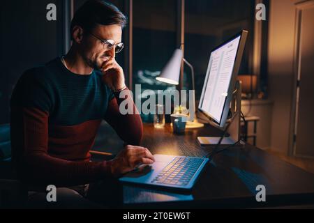 A focused, young entrepreneur works late in his office, engrossed in an online meeting. He's determined, pensive, and dedicated to his business. Stock Photo