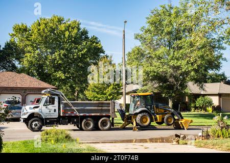 Wichita Kansas water department employee digs up a water line with John Deere backhoe with bulldozer in an urban neighborhood. Wichita, Kansas, USA. Stock Photo