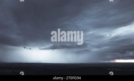 Big dark storm with sunbeams coming through them in the background. On right side is clear sky with sunset. Dark clouds rain Stock Photo
