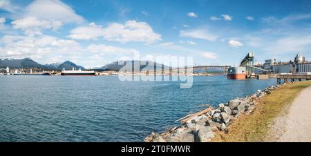 Cargo ship docked at port terminal in front of bridge and anchored container ships. Marine transport panorama with port facility. Iron workers Memoria Stock Photo