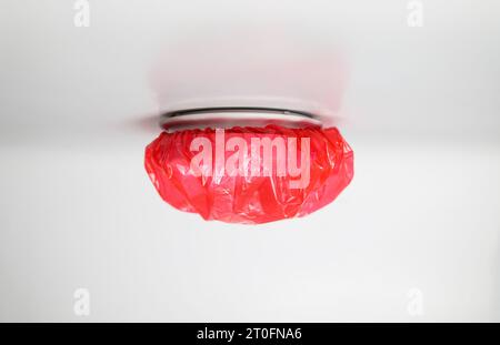 Smoke detector with dust or paint cover on ceiling. Red plastic cover used to protect smoke detector and prevent false fire alarms from excessive dust Stock Photo