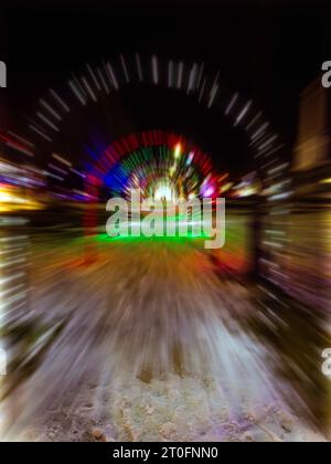 An abstract treatment of a Christmas display tunnel of illuminated arches above a snow-covered walkway achieved with radial blurring Stock Photo