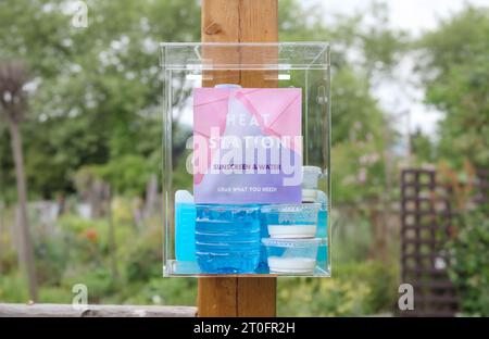 Free water and sunscreen dispensary in front of community garden. Plexiglass station with water bottles and individual sunscreen for hot sunny days. C Stock Photo