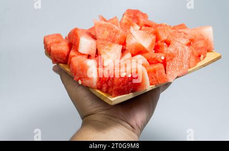 Red and fresh peeled watermelon served on a wooden plate held in the hand isolated on a white background Stock Photo