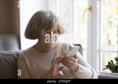 Cheerful elderly great grandma woman using mobile phone at home Stock Photo