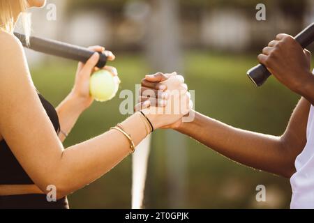 Amateur tennis players shaking hands at the net. Two sportswomen shaking hands over the net after the match. Stock Photo