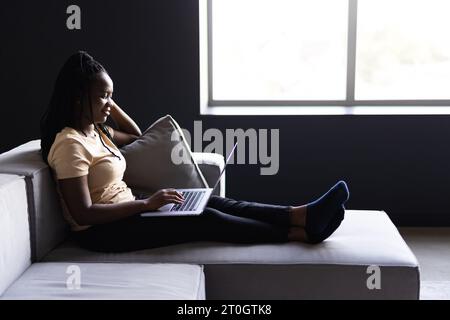 Woman sitting on living room couch working remotely from home using laptop computer. woman using laptop computer surfing the net while spending leisur Stock Photo