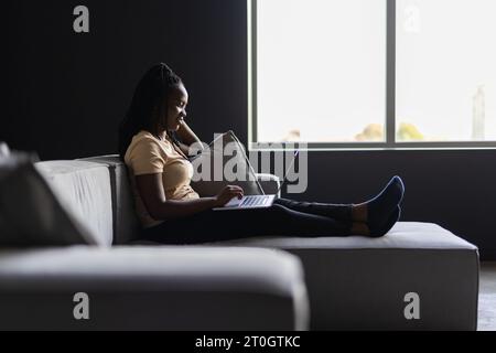 Woman sitting on living room couch working remotely from home using laptop computer. woman using laptop computer surfing the net while spending leisur Stock Photo