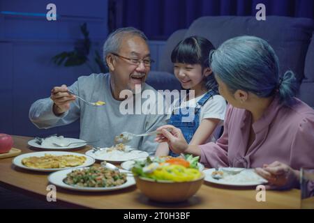 family grandmother grandfather and granddaughter dining on table and having fun during Stock Photo