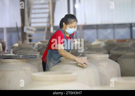 CHONGQING, CHINA - OCTOBER 7, 2023 - A worker colors a wine jar with flowers in a ceramic production workshop on October 7, 2023, Chongqing, China. Stock Photo