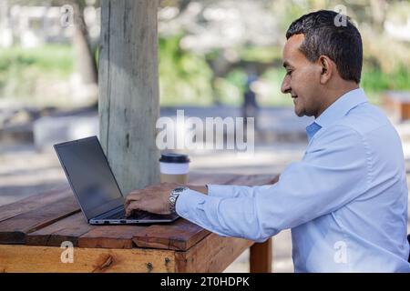 Young Latino man using a laptop outdoors with copy space. Stock Photo