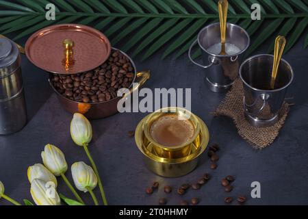 South Indian Filter coffee served in a traditional brass tumbler or cup with roasted raw coffee beans. Traditional Filter coffee served in a brass cup Stock Photo