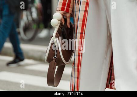 A guest wearing a checkered trench coat, white pants, a tie and brown bag, seen outside PRADA show during Milan Fashion Week Womenswear Spring/Summer Stock Photo