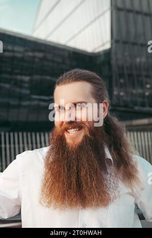 Man portrait Scandinavian european thirty years old long bearded with long red hair hairdresser barber positive cheerful smiling white teeth in white shirt. concept barbershop  Stock Photo