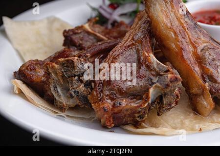 Fried Ribs on a white plate with sauce and onions Stock Photo