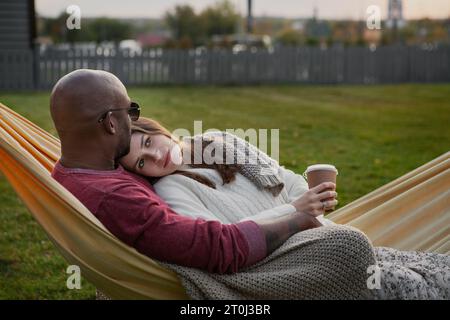 Beautiful couple in love, wrapped in cozy blanket, embracing while lounging in hammock amidst beauty of nature park. Cherished moments together. Tranq Stock Photo