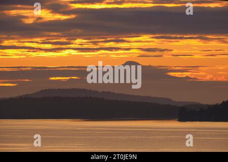 Before sunrise a beautiful orange sky streaked with clouds and Mt Baker 130 km away as seen over the water from Vancouver Island. Stock Photo