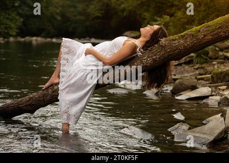 beautiful woman in white dress lying on a log on the river bank Stock Photo  - Alamy