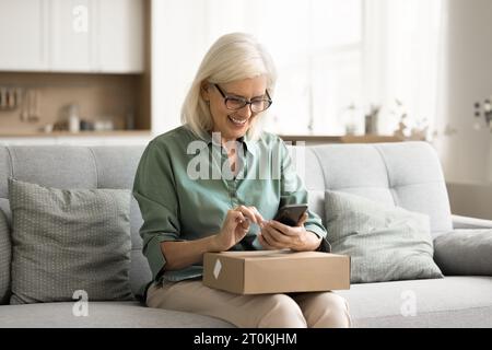 Cheerful old retired consumer woman getting purchase from Internet store Stock Photo