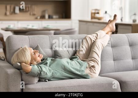 Joyful carefree retired woman enjoying relaxation on soft comfortable sofa Stock Photo