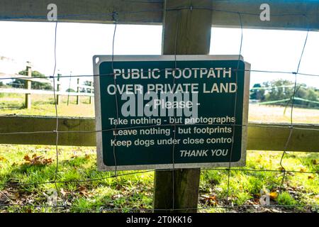 A green sign attached to a wooden fence stating rules when walking along a public footpath over private land Stock Photo