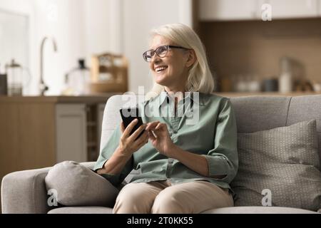 Happy positive older blonde woman in eyewear holding smartphone Stock Photo
