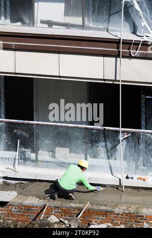 On a sunny day, construction workers are laying cement for the road next to the residential building under construction. Stock Photo