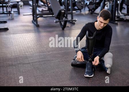 young male athlete putting on sneakers on his artificial leg, disabled guy ties his shoes. close up photo. copy space Stock Photo
