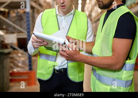 Caucasian two engineers in uniform, checking goods and supplies on shelves in warehouse. logistic and business export. Concept of good management syst Stock Photo