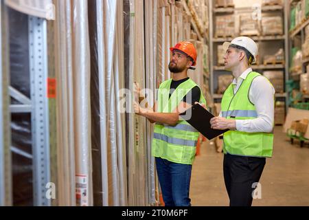 confidentmale warehouse workers in working clothes talking together in warehouse, caucasian men counting goods in shelves, controlling the disctributi Stock Photo