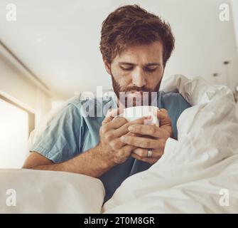 Tea, sick and a man with a blanket on a sofa in the living room of his home for recovery from cold or flu. Coffee, healthcare or lemon and ginger Stock Photo