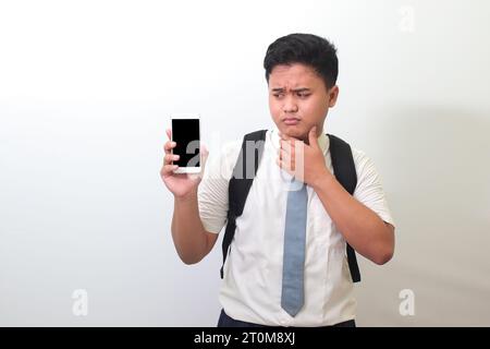 Indonesian senior high school student wearing white shirt uniform with gray tie showing and presenting blank screen mobile phone. Isolated image on wh Stock Photo