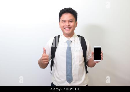 Indonesian senior high school student wearing white shirt uniform with gray tie showing and presenting blank screen mobile phone. Isolated image on wh Stock Photo