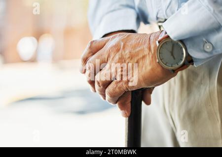Senior, hands and stand with cane in closeup for retirement, vacation or trip on blurred background. Elderly, person and wrinkles with health, medical Stock Photo