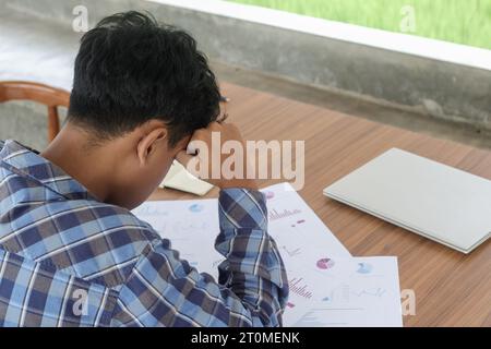 Back view close up of freelance male feeling confused and frustrated while looking down into official document, signing contract and tax. Holding his Stock Photo