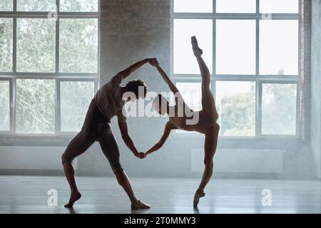 Silhouette of man and woman ballet dancers performing together against studio background Stock Photo